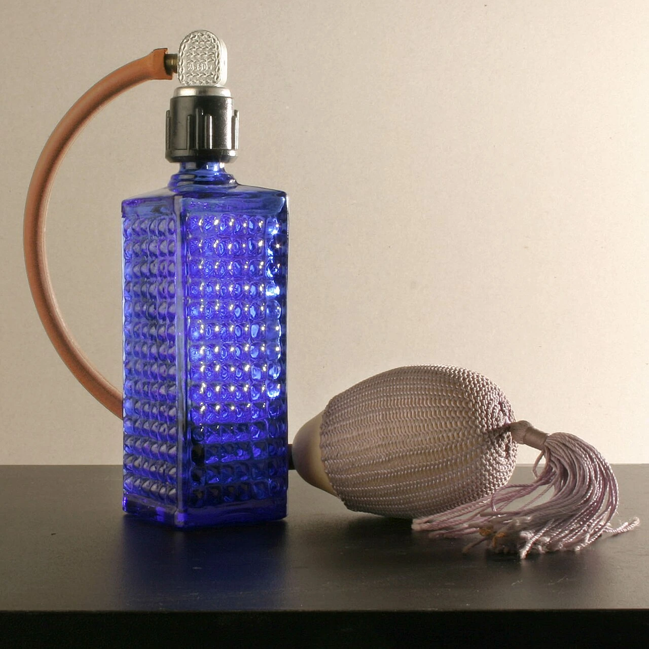 A blue glass perfume bottle with a silver cap and bulb atomizer on a table