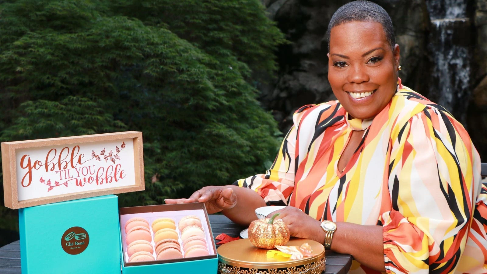 Finia Jahangard smiling beside a box of colorful macarons in an outdoor editorial-style portrait.