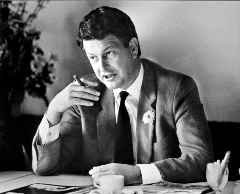 Black-and-white portrait of Kommer Damen seated at a table, holding a cigarette