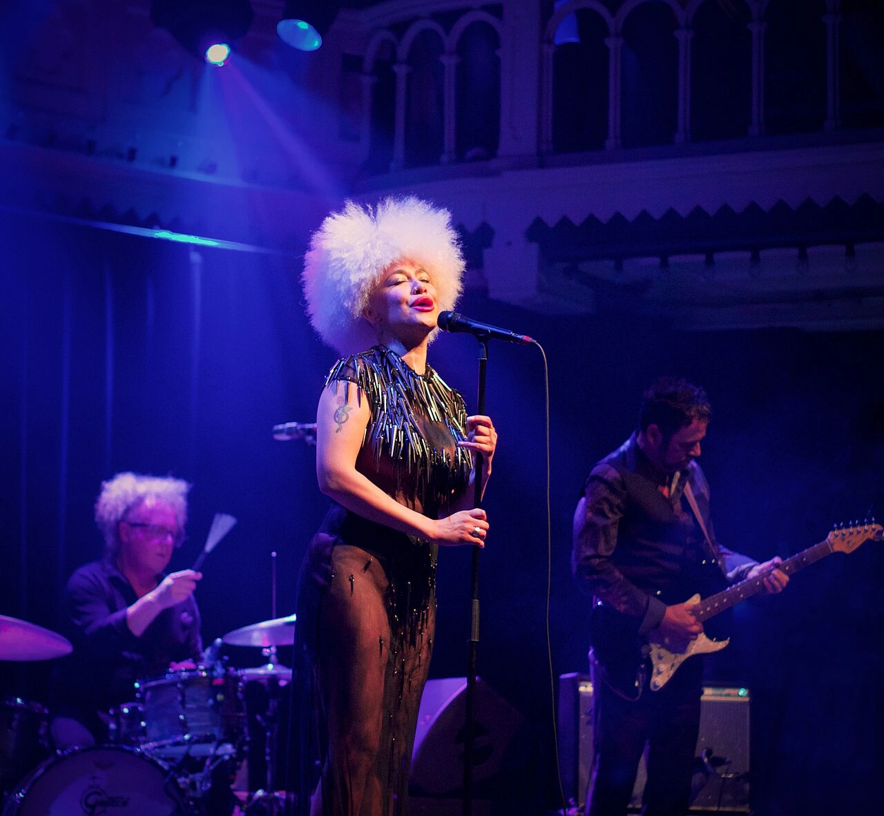 Lady Blackbird performing on stage under purple lighting with band members behind her
